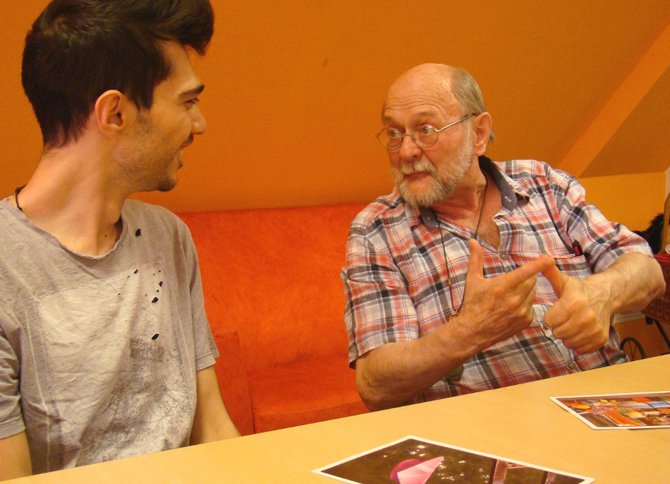 Gespräch eines jungen und eines alten Mannes mit Gestik am Tisch mit Bildern
